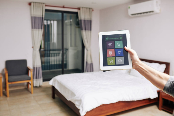 Mężczyzna korzystający z aplikacji smart home do sterowania światłem, temperaturą i wideomonitoringiem w swoim pokoju - Zdjęcie, obraz