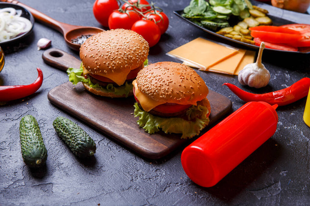 Photo of two hamburgers, chili peppers, cheese, tomato on black table - Photo, Image