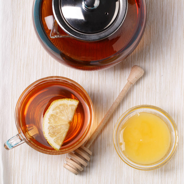 Glas Tee mit Zitrone, Glas Teekanne und Honig auf blauem Holztisch. - Foto, Bild