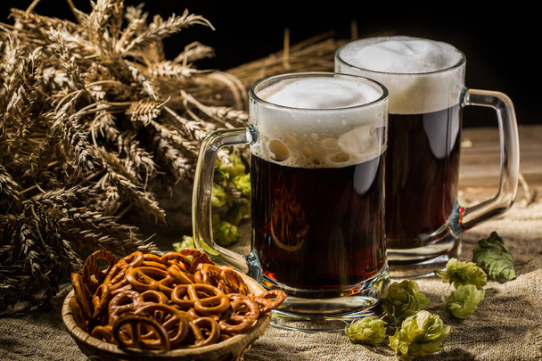 Dos cervezas cisterna con trigo y lúpulo, canasta de pretzels sobre mesa de madera
 - Foto, Imagen