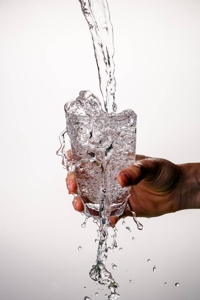 Foto de la mano con vidrio con agua que vierte, salpicaduras en el fondo gris vacío
 - Foto, imagen