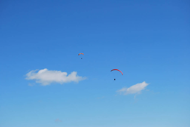 Beautiful paraglider in a blue summer sky. Sportsman flying on a paraglider, extreme sports in the air - Photo, Image