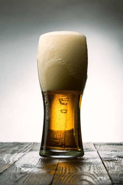 Παγωμένο ποτήρι ελαφριάς μπύρας σε ξύλινο τραπέζι και γκρι φόντο - Φωτογραφία, εικόνα