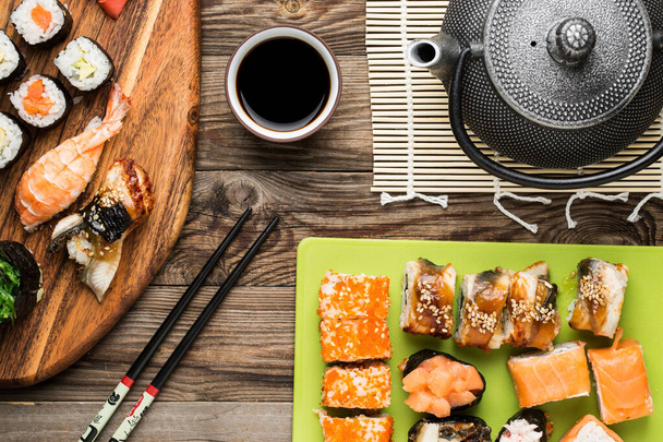 Joukko sushi rullina, syömäpuikot, soijakastike ja teekannu, tarjoillaan perinteistä japanilaista ruokaa
 - Valokuva, kuva