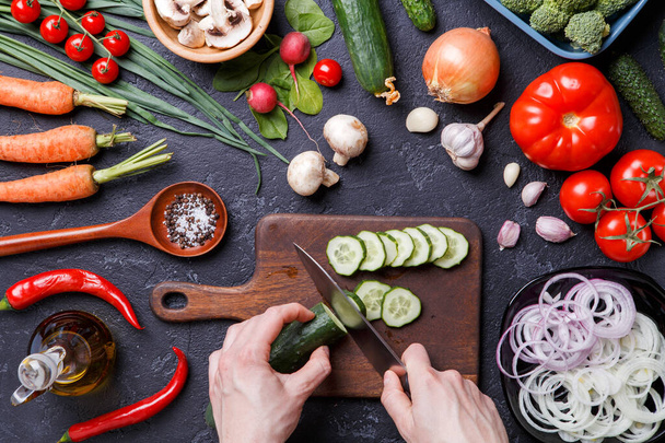 Image on top of fresh vegetables, mushrooms, cutting board, oil, knife, hands of cook on table - Photo, Image