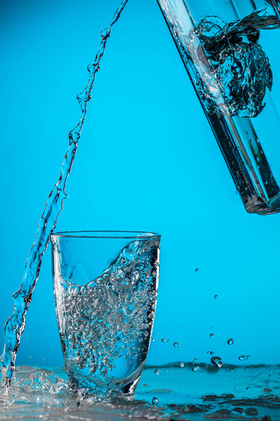 Mann gießt im Atelier Wasser aus Glas in Glas auf blauem Hintergrund - Foto, Bild