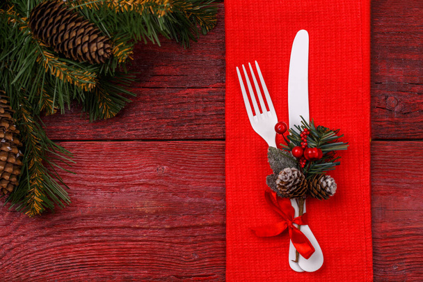 Christmas table place setting with red napkin, white fork and knife, decorated sprig of mistletoe and christmas pine branches. Christmas holidays background. - Photo, Image
