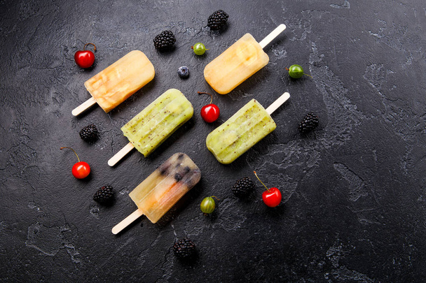 Фото замороженного сока на палочке, ежевике, вишне, крыжовнике на черном фоне
 - Фото, изображение