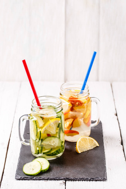 Two mugs of infused detox diet refreshing waters - first with cucumber and lemon, second with lemon and peach on white wooden table - Фото, зображення