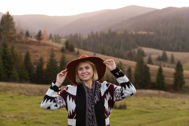 Stylish hipster traveling woman wearing  authentic boho chic style poncho and hat in autumn landscape. Happy young woman exploring sunny mountains. Travel and wanderlust concept. - Fotografie, Obrázek