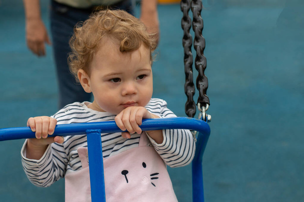 The little girl rides on a swing. Caucasian baby kid with curls on the playground - Fotó, kép