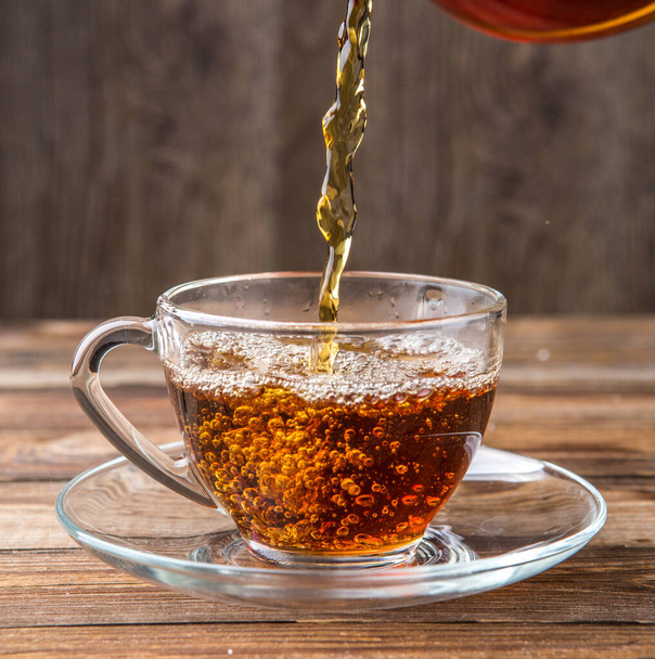 Fotografie schenkt thee in beker op houten tafel - Foto, afbeelding