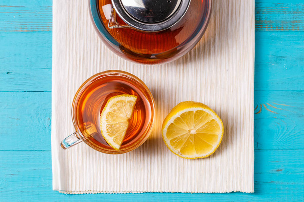 Taza de té de vidrio con limón y tetera de vidrio sobre mesa de madera azul
. - Foto, imagen