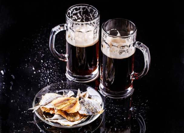 Photo of two mugs of beer with plate of fish on ablack table - Φωτογραφία, εικόνα