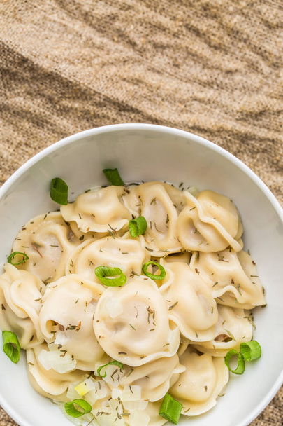 Meat dumplings - russian pelmeni, ravioli with meat on a white plate on a wooden background - Photo, Image