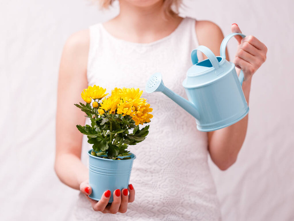 Zdjęcie kobiety trzymającej garnek z żółtym kwiatem i konewką, zbliżenie - Zdjęcie, obraz