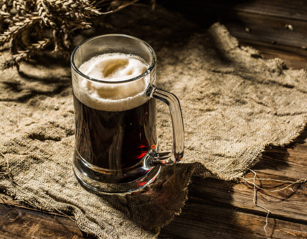 Taza de cerveza con trigo sobre tela de lino sobre mesa de madera
 - Foto, Imagen