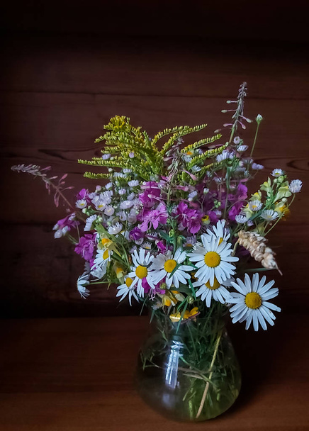 Tahta bir arka planda, cam bir vazoda parlak yabani çiçeklerden oluşan güzel bir buket - Fotoğraf, Görsel