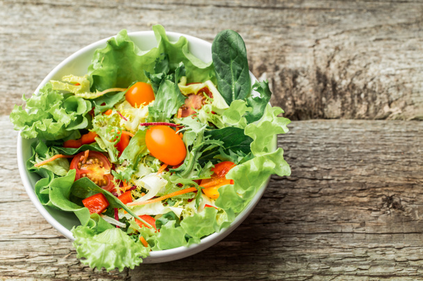 Salade met verse groenten - tomaten, wortelen, paprika en gemengde Groenen - rucola, mesclun, mache - op houten achtergrond. - Foto, afbeelding
