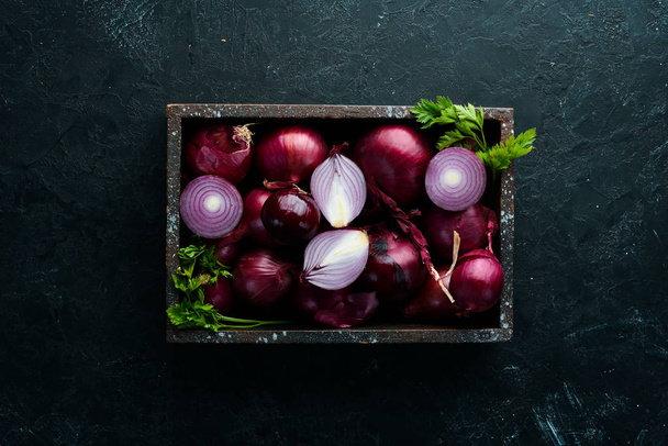Purple onion in wooden box on black background. Top view. Free copy space. - Foto, afbeelding