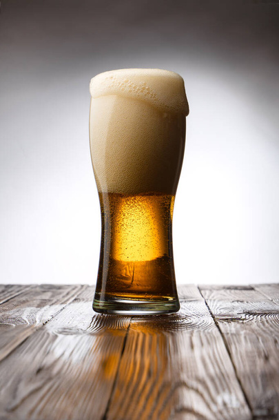Frosted glass of light beer on wood table and white background behind - Фото, изображение