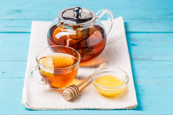 Glas Tee mit Zitrone, Glas Teekanne und Honig auf blauem Holztisch. - Foto, Bild