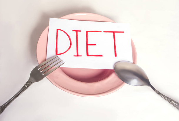 Słowo dieta jest napisane na białym arkuszu, który leży na pustym talerzu z urządzeń - Zdjęcie, obraz
