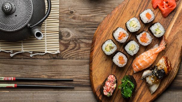 köstliche frische Brötchen, Sushi und Gunkan mit Essstäbchen und Teekanne auf natürlichem Holzgrund - Foto, Bild