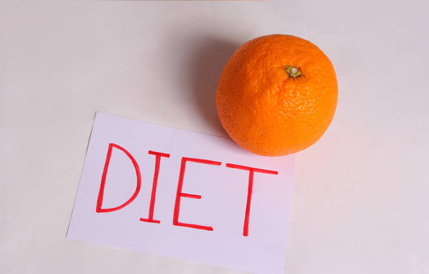 Слово диета написано на белом листе с апельсином на светлом фоне
 - Фото, изображение