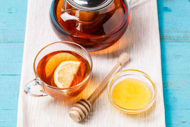 Taza de té de vidrio con limón, tetera de vidrio y miel en la mesa de madera azul
. - Foto, Imagen