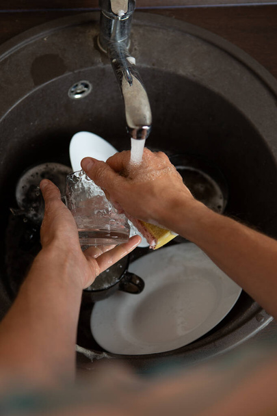 Изображение сверху человеческих рук, вымывающих посуду в раковину на кухне
 - Фото, изображение