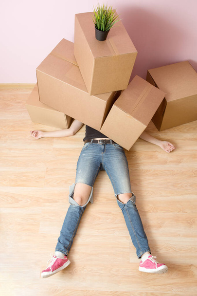 Photo of woman in jeans lying under cardboard boxes in new apartment - Photo, Image
