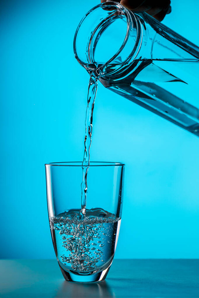 El hombre vierte agua del vidrio en vidrio sobre fondo azul en el estudio
 - Foto, Imagen