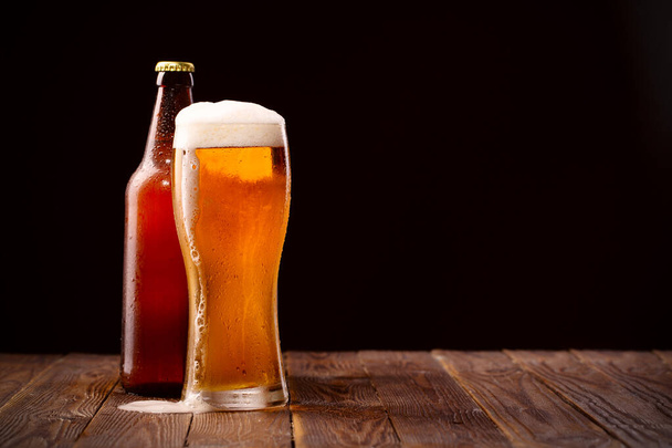 Photo of buttle and glass of beer at table and black background behind - Foto, afbeelding
