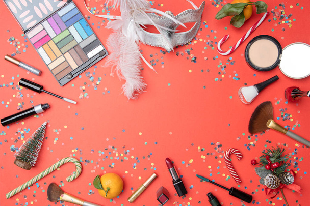 Photo on top of eye shadows, brushes, feather mask, tangerine, sugar cane,confetti on empty red table, place for inscription - 写真・画像