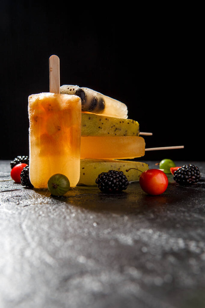 Photo of fruit ice from berries on stick, blackberry, cherry, gooseberry on black background - Photo, image