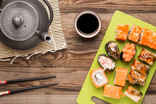 Ассорти вкусные свежие японские роллы с соевым соусом, палочкой для еды и чайником
 - Фото, изображение