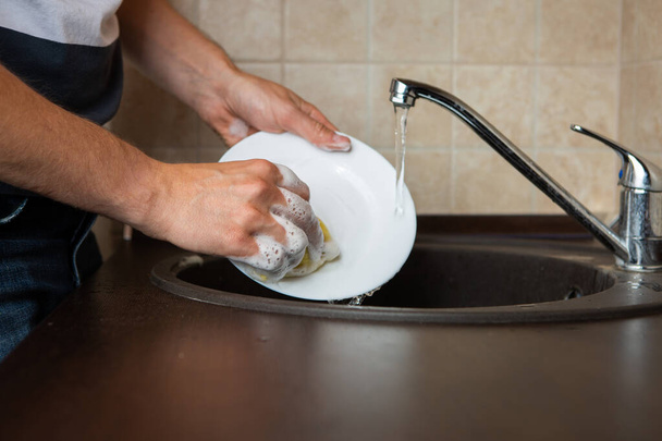 Photo of side of man's hands washing transparent mug in sink in kitchen - Photo, Image