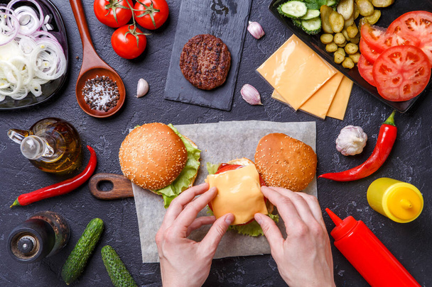Image on top of two hamburgers, human hands and ingredients on black table - 写真・画像