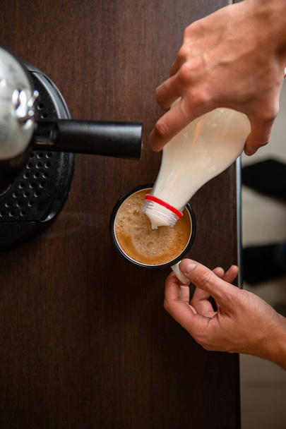 Image d'une cafetière, les mains de l'homme versant du lait dans une tasse de café dans la cuisine
 - Photo, image