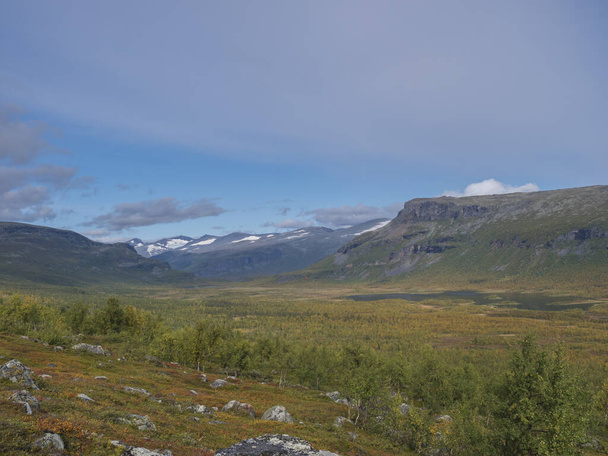 Beautiful wild nature of Sarek national park in Sweden Lapland with snow capped mountain peaks, river and lake, birch and spruce tree forest. Early autumn colors, blue sky white clouds. - Fotoğraf, Görsel