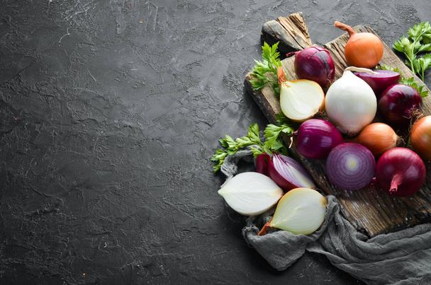 Colored ripe onions on wooden board on black background. Top view. Free copy space. - 写真・画像