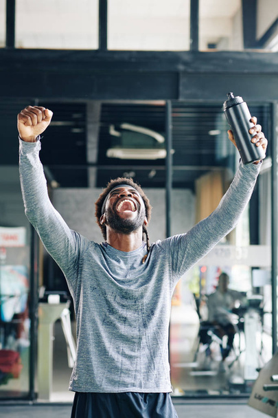 Nadšený šťastný fit muž hrdý na sebe po dosažení nového cíle v tělocvičně - Fotografie, Obrázek