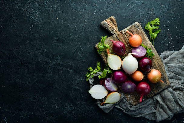 Colored ripe onions on wooden board on black background. Top view. Free copy space. - 写真・画像