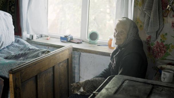 Lovely grandmother sitting by the window with a cat in an old house. Traditional old house lonely old woman in western Ukraine - Foto, Bild