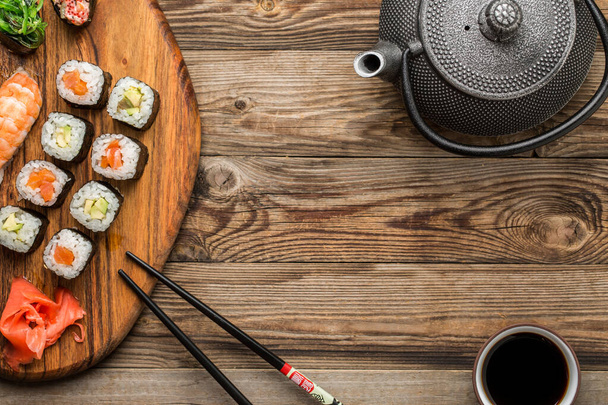 Closeup of rolls with soy sauce and black sticks on bottom, top view, wooden background - Photo, Image
