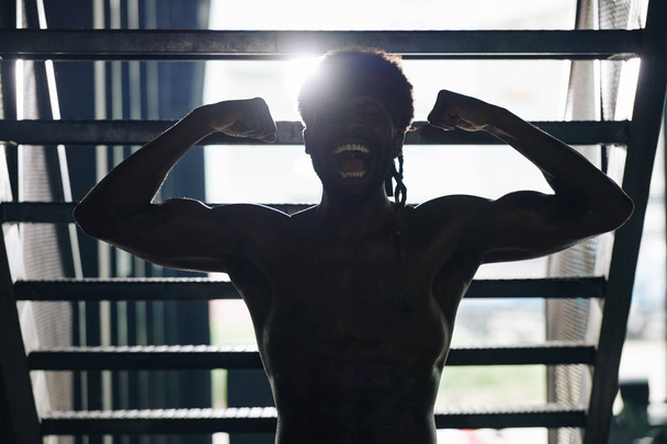 Młody, umięśniony sportowiec krzyczący i pozujący do pokazania muskulatury ramion bicepsa, podświetlony - Zdjęcie, obraz