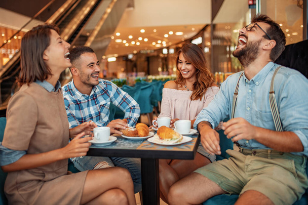 Група друзів, які мають каву разом. Молоді чоловіки і жінки сидять за столом кафе і посміхаються
. - Фото, зображення