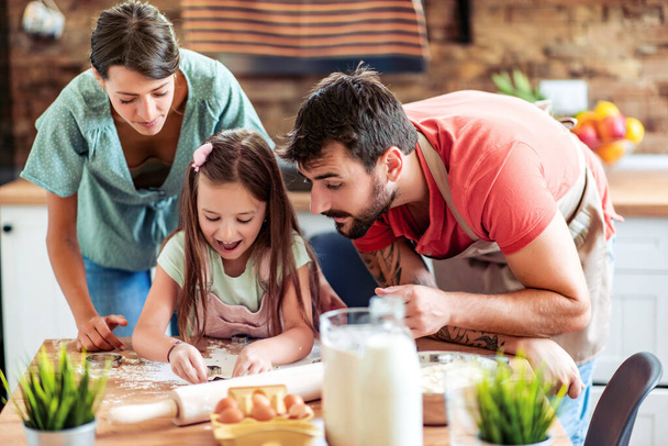 Щаслива сім'я на кухні. мати, батько і дочка готують тісто, роблять випічку
. - Фото, зображення