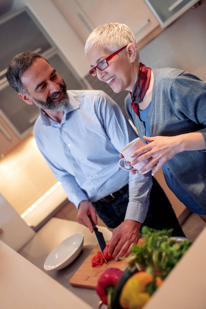 Πορτρέτο του ευτυχισμένου ώριμου ζευγαριού κάνοντας σαλάτες μαζί στην κουζίνα τους. - Φωτογραφία, εικόνα